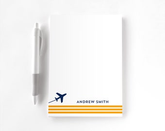May include: White notepad with a blue airplane graphic and three yellow stripes at the bottom. The text "ANDREW SMITH" is printed below the airplane.