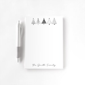 May include: A white notepad with a black pen. The notepad features a row of five black and white Christmas tree illustrations at the top. The words "The Smith Family" are written in a script font at the bottom.