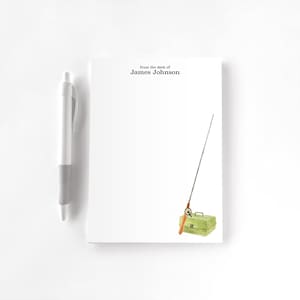 May include: White notepad with the text "from the desk of James Johnson" and a watercolor illustration of a fishing rod and tackle box. A white pen rests on the left side of the notepad.