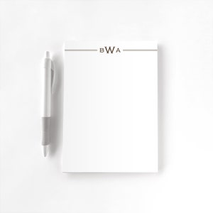 May include: A white notepad with a brown line and the letters "BWA" printed on the top. A white pen is next to the notepad.