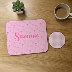 May include: A pink mousepad and coaster set with a bow pattern and the name "Sammie". The mousepad is rectangular with rounded corners. A small succulent plant in a white pot and a cup of coffee are also visible.