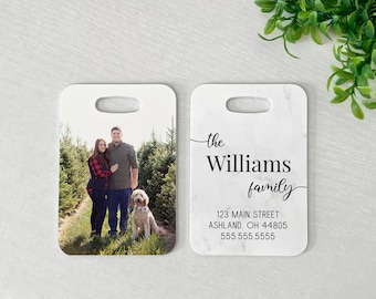 May include: Two people and a dog stand in front of a Christmas tree farm. The couple is holding hands and smiling. The dog is a golden retriever. The text on the cutting board reads "The Williams Family, 123 Main Street, Ashland, OH 44805, 555.555.5555".