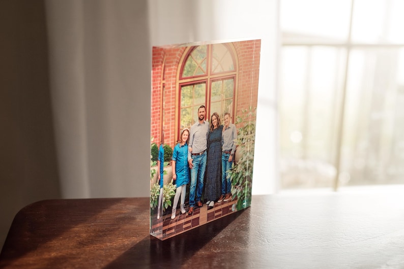 May include: A family of four poses for a photo in front of a brick building with a large arched window. The family is wearing blue clothing and smiling. The photo is printed on a clear acrylic block.
