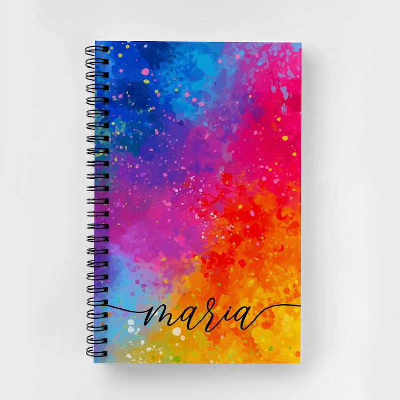 May include: A colorful spiral notebook with a watercolor background in shades of blue, purple, red, orange, and yellow. The notebook has the name "maria" written in black cursive on the front.