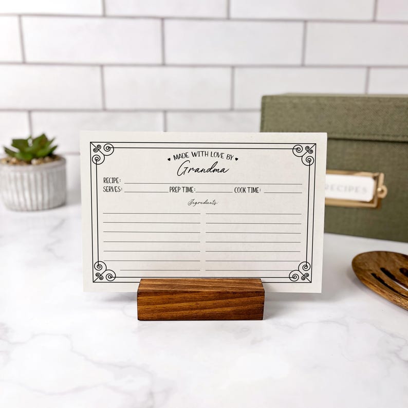 May include: A white recipe card with a black border and the text "MADE WITH LOVE BY Grandma" in a decorative font. The card has spaces for the recipe name, servings, prep time, cook time, and ingredients.