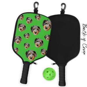 May include: Pickleball paddle with a green face featuring multiple dog faces. The back of the paddle is black. A green pickleball and a black handle are also visible. The text "Back of Cover" is printed on the side.