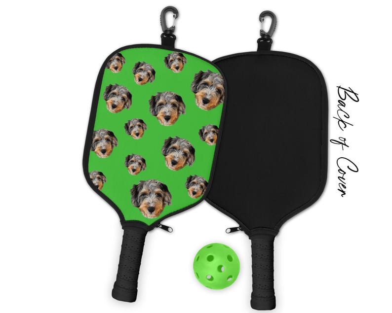 May include: Pickleball paddle with a green face featuring multiple dog faces. The back of the paddle is black. A green pickleball and a black handle are also visible. The text "Back of Cover" is printed on the side.