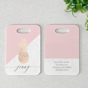 May include: Two pink luggage tags with a gold pineapple design. One tag has the name "jenny" written in cursive. The other tag has the text "jennifer smith, 123 davis rd., ashland, oh 44805, 419.555.0123".