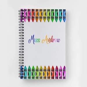 May include: A spiral bound notebook with a white cover and a rainbow border of crayon drawings. The text "Miss Andrew" is written in rainbow colors on the cover.