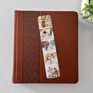 May include: A brown leather-bound journal with a patterned spine, and a photo bookmark. The bookmark displays a series of family photos. A small potted plant and woven basket are in the background.
