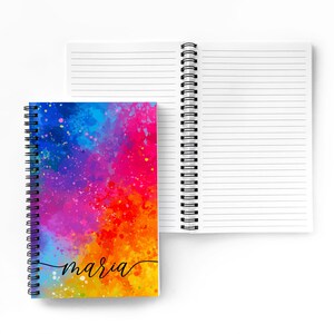 May include: A spiral bound notebook with a colorful watercolor design on the front cover. The design features a rainbow of colors with splashes of paint. The name "maria" is written in black cursive on the front cover.