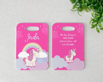 May include: Two pink luggage tags with a unicorn and rainbow design. The tag on the left says "Jada" and the tag on the right says "This bag belongs to Jada Smith. If found, please call 419-555-0001."