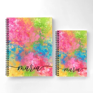 Puede incluir: Dos cuadernos de espiral con dise&ntilde;os abstractos de pintura salpicada de colores. El cuaderno m&aacute;s grande tiene el nombre "maria" escrito en cursiva negra en la portada. El cuaderno m&aacute;s peque&ntilde;o tiene el mismo dise&ntilde;o y el nombre "maria" escrito en cursiva negra en la portada.