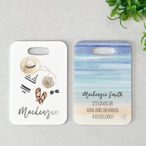 Peut inclure: Deux étiquettes à bagages sur le thème de la plage. Une étiquette présente une scène de plage de style aquarelle avec des rayures bleues et blanches. L'autre étiquette présente un fond blanc avec un chapeau de paille, un maillot de bain, des sandales et des lunettes de soleil. Les deux étiquettes portent le nom "Mackenzie". L'étiquette avec la scène de plage porte également le texte "Mackenzie Smith, 123 Davis Dr., Ashland, OH 44805, 419.555.0001".