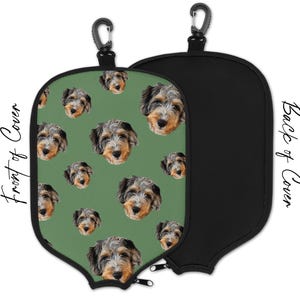 May include: A golf club cover with a repeating pattern of dog faces on a green background. The back of the cover is solid black. Includes a black carabiner clip for easy attachment.