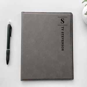 May include: Gray faux leather journal with a black embossed initial "S" and the name "TY STEVENSON" on the front cover.