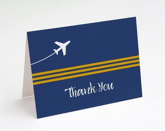 Könnte beinhalten: Eine dunkelblaue, gefaltete Grußkarte mit einer weißen Flugzeuggrafik samt Kondensstreifen, zwei horizontalen goldenen Streifen und dem weißen Schriftzug Thank You in Schreibschrift auf der Vorderseite.