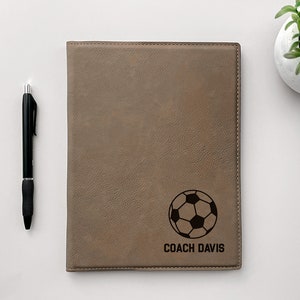 May include: Brown leatherette notebook with a soccer ball and the text "COACH DAVIS" engraved on the front.