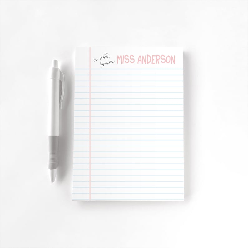 Puede incluir: Bloc de notas blanco con l&iacute;neas azules y margen rosa. El texto "a note from MISS ANDERSON" est&aacute; impreso en rosa. Un bol&iacute;grafo blanco y gris descansa a la izquierda. Papeler&iacute;a para notas.
