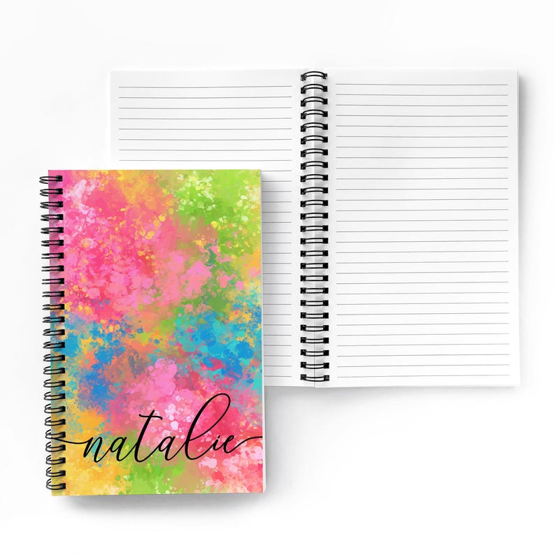 Puede incluir: Un cuaderno de espiral con un dise&ntilde;o abstracto colorido en la portada. El dise&ntilde;o presenta una mezcla de colores rosa, azul, amarillo y verde. El nombre "natalie" est&aacute; escrito en cursiva negra en la portada.