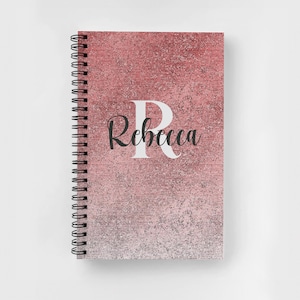 May include: A pink and white glitter notebook with a spiral binding. The notebook has the letter "R" and the name "Rebecca" printed on the front.