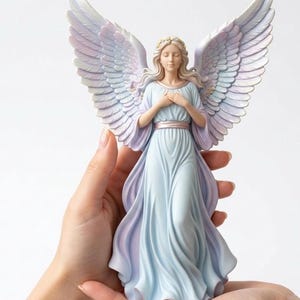 Op de afbeelding: Een serene engelenfiguur met uitgestrekte vleugels. De engel draagt een vloeiende, lichtblauwe jurk met een bijpassende sjerp. De vleugels hebben een verloop van wit, lavendel en lichtblauw. De engel heeft blond haar en een gouden kroon.