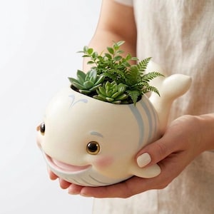 Puede incluir: Una taza de cerámica blanca con un asa negra y el texto "But First, Coffee" en negrita negra. La taza se encuentra sobre un fondo borroso, sugiriendo un ambiente acogedor.