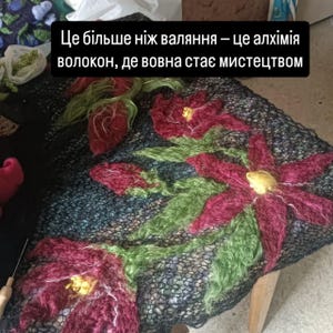 Pu&ograve; includere: Tessuto fatto a mano con sfondo scuro, ornato da grandi e vibranti disegni floreali rossi e verdi. I fiori hanno centri gialli. Il testo nell'immagine recita: "Questo &egrave; pi&ugrave; che feltro - &egrave; l'alchimia delle fibre, dove diventa arte."