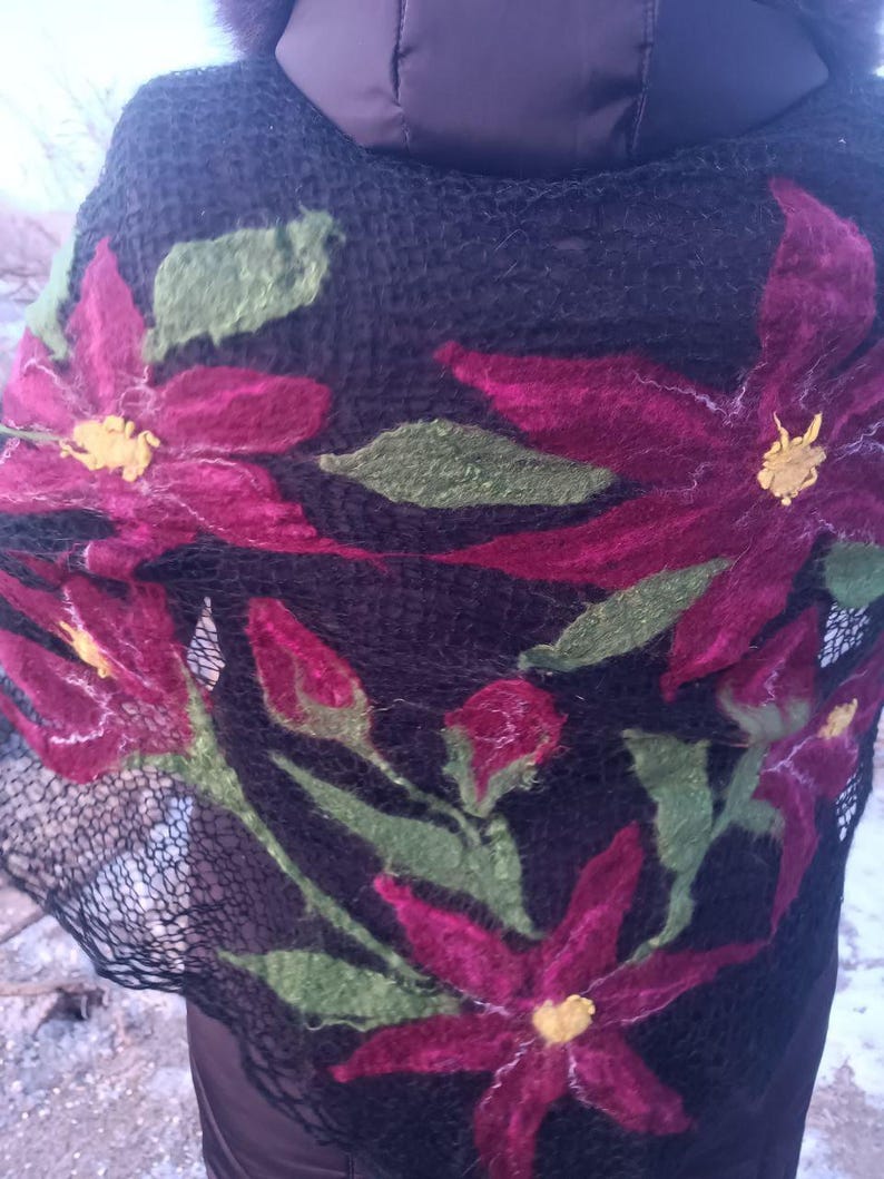 Pu&ograve; includere: Sciarpa nera con grandi fiori magenta in feltro, foglie verdi e centri gialli. Il motivo floreale &egrave; cucito a mano sul tessuto a trama aperta. La sciarpa &egrave; drappeggiata sulle spalle di una persona, mostrando gli intricati dettagli dell'arte tessile.