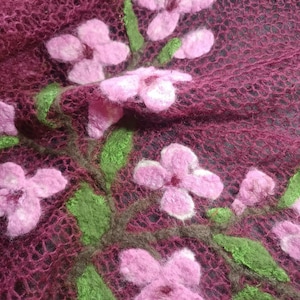 Pu&ograve; includere: Primo piano di un tessuto bordeaux a trama aperta, ornato da fiori rosa infeltriti e foglie verdi. I fiori, con centri bianchi, sono disposti in un motivo floreale. Il tessuto ha un aspetto delicato e arioso, che suggerisce una sciarpa o uno scialle.