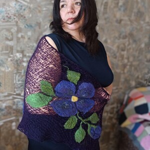 Pu&ograve; includere: Uno scialle viola scuro con un grande fiore blu ricamato e foglie verdi. Lo scialle ha una trama a rete ed &egrave; drappeggiato sulle spalle. Il fiore ha un centro giallo.