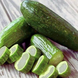 Può includere: Diversi cetrioli verdi freschi, alcuni interi e altri tagliati, sono disposti su una superficie di legno. I cetrioli hanno una buccia verde scuro con macchie bianche. I cetrioli a fette rivelano un interno bianco. L'immagine mostra un alimento sano.