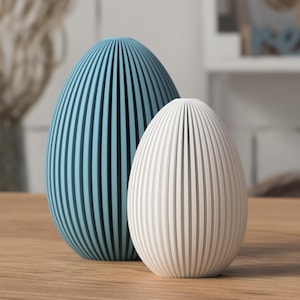 May include: Two decorative egg-shaped objects. One is light blue, the other is white. Both have vertical grooves. They are placed on a wooden surface. The objects are likely for home decor.