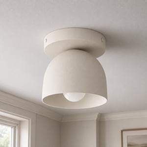 Könnte beinhalten: Eine matte beige Deckenleuchte zur direkten Montage mit einem kuppelförmigen Schirm. Die Leuchte verfügt über eine kreisförmige Basis an der Decke und eine einzelne, sichtbare weiße Glühbirne, die mittig in der nach unten gerichteten Kuppel sitzt.