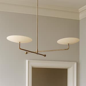 May include: A modern, brass-toned chandelier with two oval, frosted glass shades. The fixture has a minimalist design, with a central rod and horizontal arms extending to hold the shades. The light fixture is suspended from the ceiling.