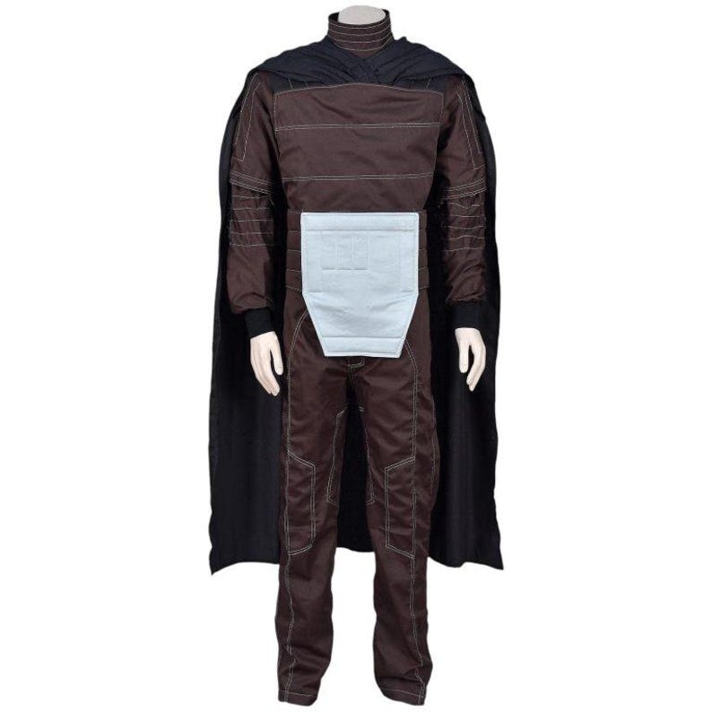 May include: A dark brown jumpsuit featuring a high collar, long sleeves, and visible white stitching throughout. A light gray rectangular panel is centered at the waist. A long, solid black cape is attached at the shoulders and hangs down the back.