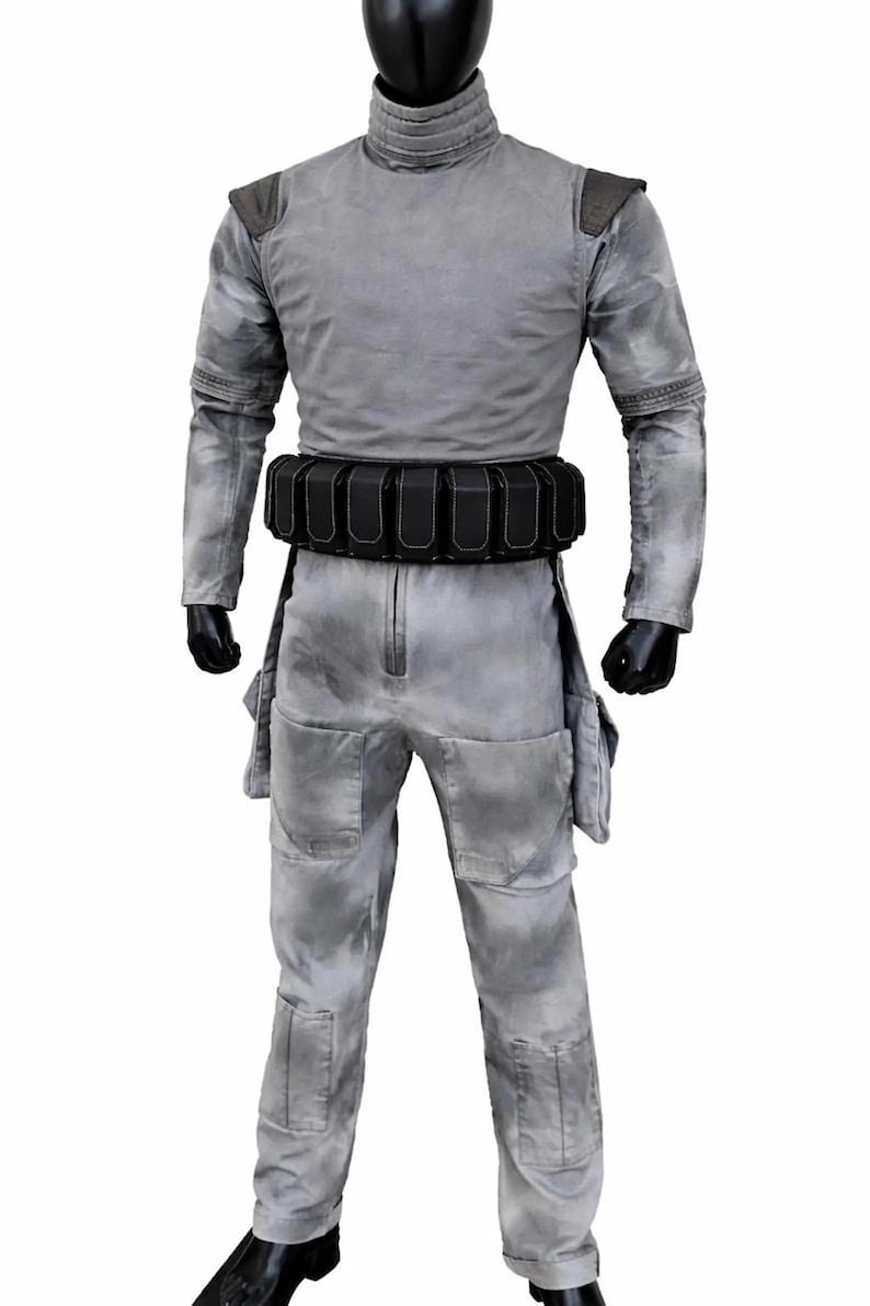 May include: A grey jumpsuit with a mottled, weathered texture, featuring a high collar, long sleeves, and dark shoulder patches. A black utility belt with multiple rectangular pouches is worn around the waist. The garment includes large thigh pockets.
