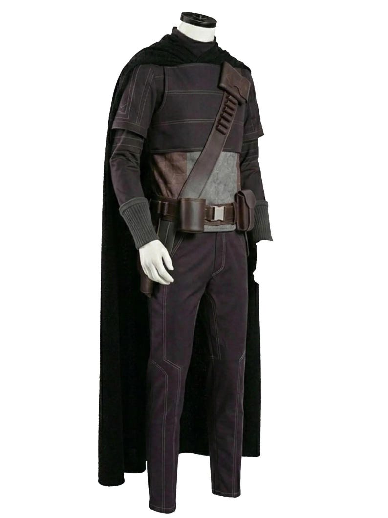 K&ouml;nnte beinhalten: Ein dunkelvioletter Anzug mit einem schwarzen Umhang. Das Outfit umfasst ein lang&auml;rmeliges Hemd, eine Hose und einen G&uuml;rtel mit Taschen. Das Kost&uuml;m hat ein futuristisches Design mit einem braunen Lederriemen &uuml;ber der Brust.