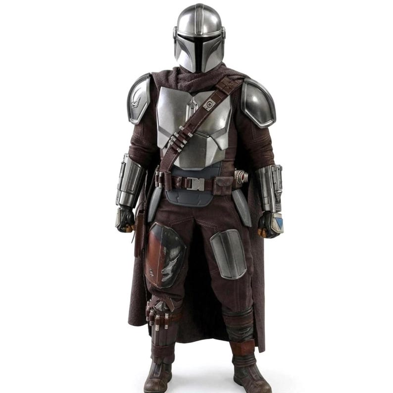May include: A collectible action figure of a warrior wearing a metallic silver helmet and chest armor over a dark brown fabric suit. The figure features shoulder pauldrons, gauntlets, a utility belt with a diagonal strap, and a long brown cape.