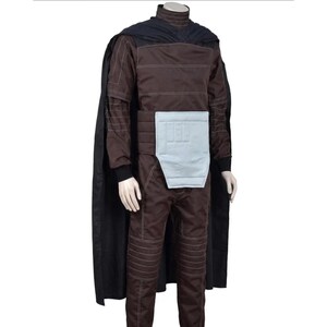 May include: A dark brown jumpsuit featuring a high collar, long sleeves with white stitching, and ribbed detailing on the legs. A light gray rectangular panel is attached to the waist. A long black cape is draped over the shoulders and back.