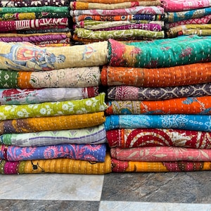 Puede incluir: Montones de colchas coloridas y estampadas. Las colchas muestran una variedad de colores, incluyendo verde, naranja, azul y rosa. Algunas colchas presentan diseños y patrones intrincados, mientras que otras tienen una apariencia más simple y sólida. Las colchas están cuidadosamente dobladas.