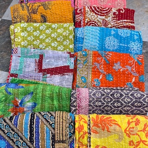 May include: A collection of colorful, folded textile blankets. The blankets feature various patterns, including floral, geometric, and abstract designs. The color palette includes shades of blue, green, yellow, orange, and pink. The blankets appear to be made of a soft, quilted material.
