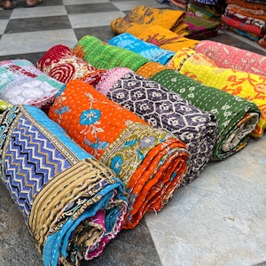 May include: A collection of rolled-up, colorful quilts with various patterns and designs. The quilts feature a range of colors, including blue, orange, green, and yellow. Each quilt is tightly rolled, showcasing the intricate patterns and textures of the fabric.