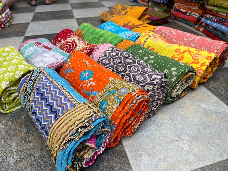 May include: A collection of rolled-up, colorful quilts with various patterns and designs. The quilts feature a range of colors, including blue, orange, green, and yellow. Each quilt is tightly rolled, showcasing the intricate patterns and textures of the fabric.