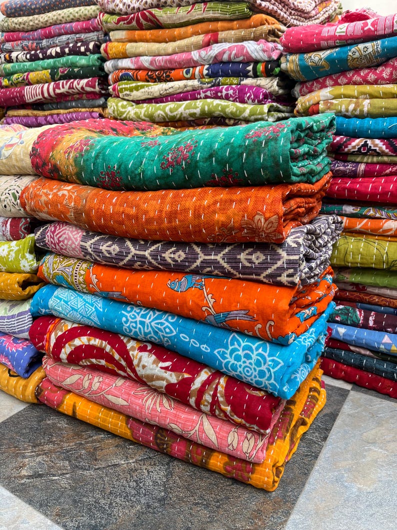 May include: A stack of colorful, rolled-up quilts. The quilts feature various patterns and colors, including orange, teal, blue, and pink. The quilts are made of fabric and have visible stitching.