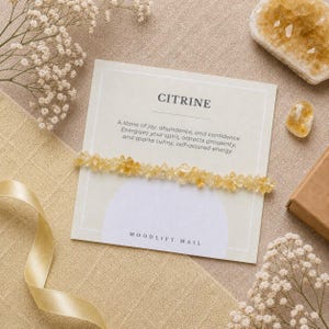May include: A citrine bracelet with a card labelled "CITRINE" detailing the stone's qualities. The bracelet is composed of small, pale yellow citrine stones. The card also features the text "MOODLIFT MAIL".