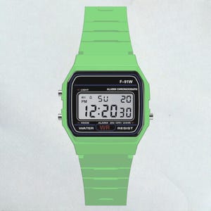 May include: A digital watch with a green band and case. The watch face displays the time, day, and date. The watch has the text "F-91W" and other function labels. The watch is water resistant.
