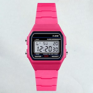 May include: A bright pink digital watch with a black display screen. The watch face displays the time, day, and date. The watch has a pink band and is labeled "F-91W".