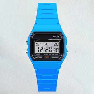 May include: A bright blue digital wristwatch with a black display. The watch face shows the time, day, and date. The watch has the text "F-91W" and "WATER WR RESIST". The watch band is also bright blue.