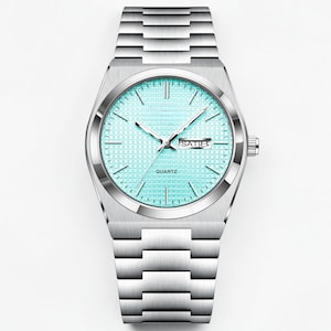 May include: A silver-toned quartz watch with a light blue face and a matching silver band. The watch face displays the day of the week and the word "QUARTZ". The watch has a rectangular case and a link-style band.
